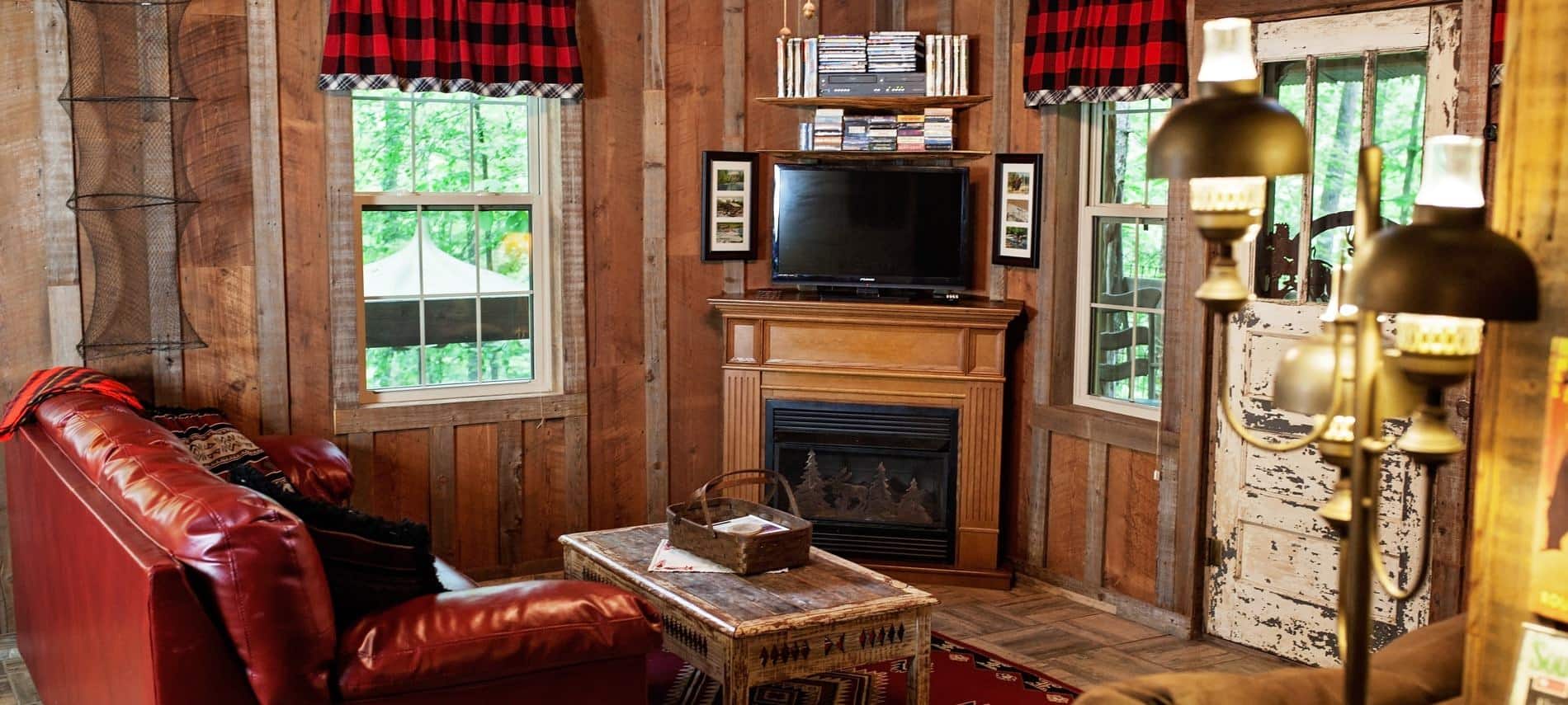 Wood cabin interior with corner fireplace, TV, several windows, and leather sofa with coffee table